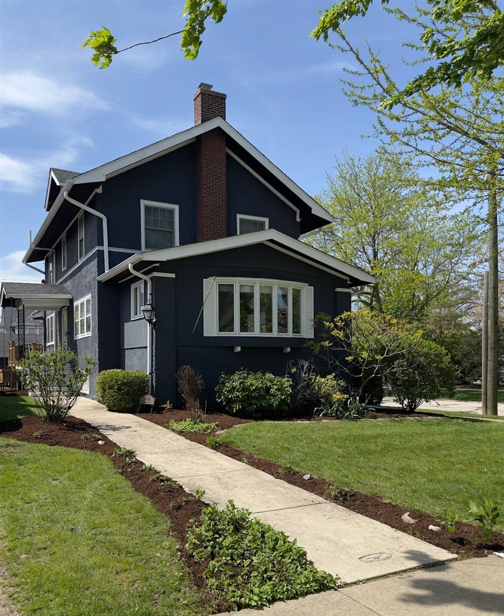 Dark blue two-story house with freshly mulched, edged beds along the front walk and a green lawn