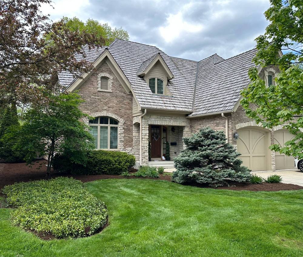 Brick and stone house with a striped green lawn, trimmed shrubs, and dark mulch around the beds and evergreen